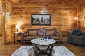 A cozy cabin interior with a wooden interior, a sofa, a coffee table, and a painting on the wall. - Pigeon Forge*Romantic*Cozy*Great for Couples (PIGEON FORGE)