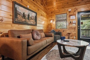A cozy cabin interior with a brown leather sofa, a round marble table, and a framed landscape painting on the wall.