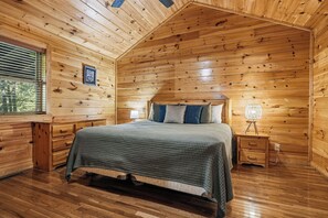 A wooden cabin bedroom with a bed, bedside tables, a lamp, and a window with blinds.
