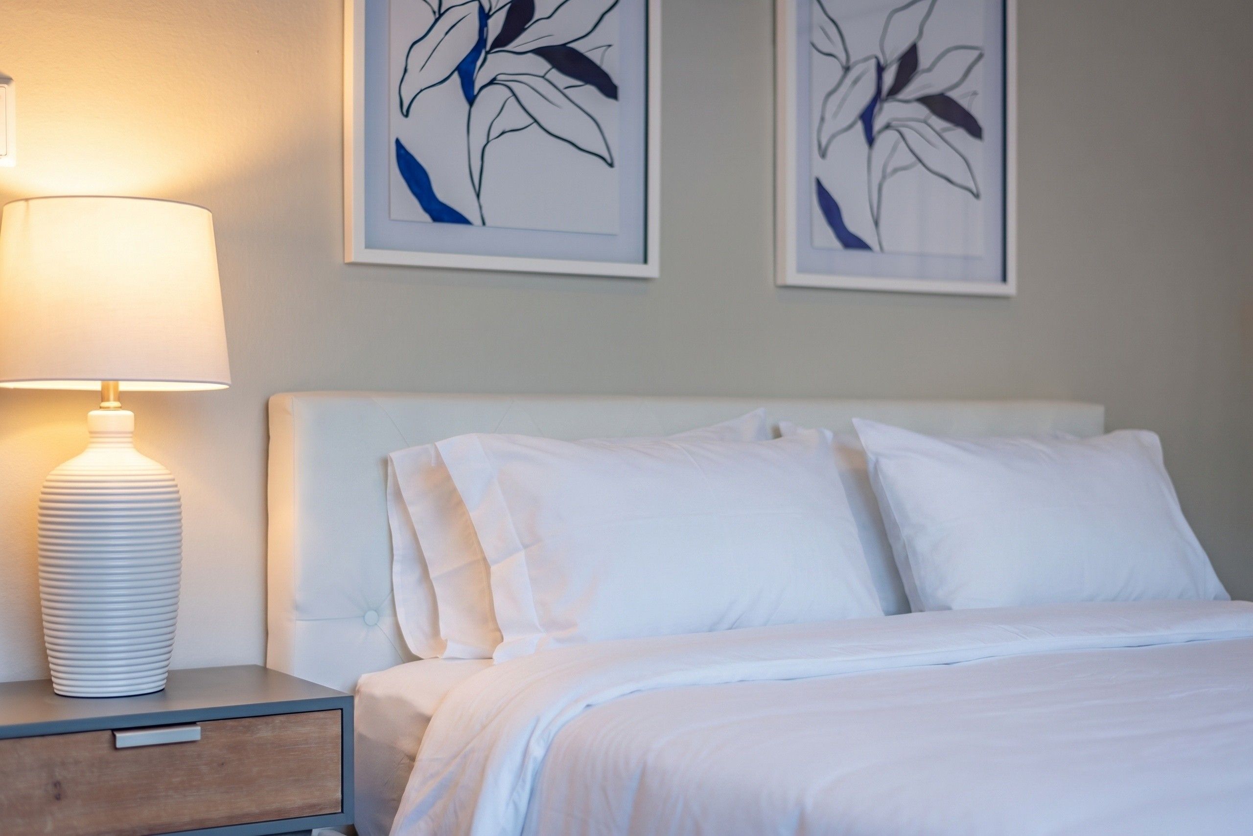 Une chambre d’hôtel comprenant un lit, une table de chevet, une lampe et deux œuvres d’art accrochées au mur.