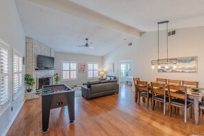 A spacious living room with a foosball table, a fireplace, a sofa, and a dining area with wooden chairs.