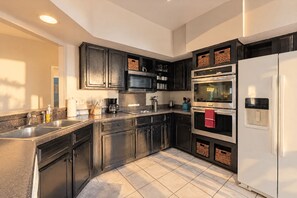 A modern kitchen with dark cabinetry, stainless steel appliances, and a tiled floor. - Peaceful North SA Retreat with Patio, Games & Community Pool (San Antonio)