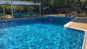 A swimming pool with clear blue water, surrounded by a covered seating area with chairs.