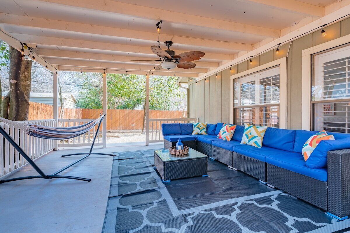 A covered patio with a blue sofa, a hammock, and a ceiling fan.