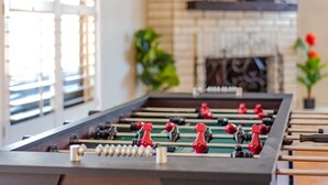 Een tafelvoetbaltafel in een kamer met een metselwerk openhaard en een televisie erboven.