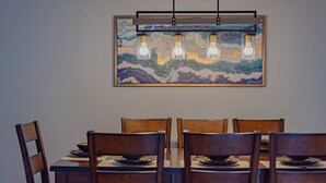 Een eetruimte met een houten tafel en stoelen, een schilderij erboven en een hanglamp met lampen.