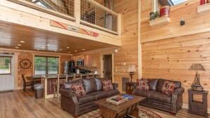 A spacious wooden cabin with a dining area, two leather sofas, a coffee table, and a kitchen in the background. - Private Pool*Home Theater w/ 4K TV (SEVIERVILLE)