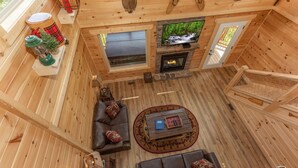 A wooden cabin interior with a fireplace, leather sofas, a television, and a wooden staircase. - Private Pool*Home Theater w/ 4K TV (SEVIERVILLE)