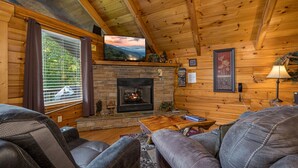 Un intérieur de chalet chaleureux avec une cheminée, des canapés en cuir, un téléviseur et des murs en bois.
