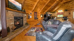 L’intérieur d’un chalet confortable, avec des murs en rondins de bois, une cheminée en pierre, des canapés en cuir et un coin cuisine.
