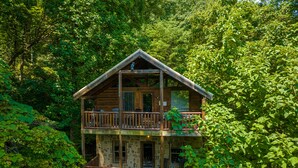 Une cabane en rondins à deux étages, dotée d’un balcon et entourée d’une forêt dense.