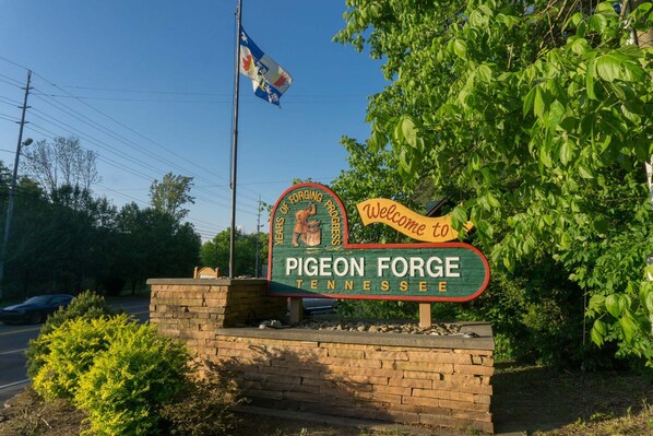 A welcome sign for Pigeon Forge, Tennessee, with a flagpole and greenery in the background.