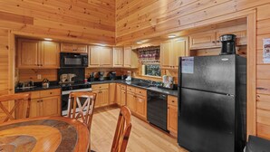A wooden-paneled kitchen with a black refrigerator, wooden cabinets, a microwave, and a dining area with a table and chairs. - NEW hot tub*Sleeps 10*In/Outdoor Fireplaces (GATLINBURG)