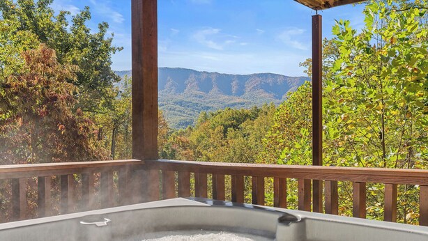 A hot tub with a wooden deck and a scenic view of mountains and trees. - NEW hot tub*Sleeps 10*In/Outdoor Fireplaces (GATLINBURG)