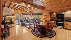 A spacious log cabin interior with a fireplace, a dining area, and a kitchen. - NEW hot tub*Sleeps 10*In/Outdoor Fireplaces (GATLINBURG)