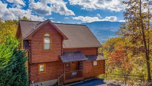 A wooden cabin with a porch, surrounded by autumn foliage and mountains in the background. - NEW hot tub*Sleeps 10*In/Outdoor Fireplaces (GATLINBURG)