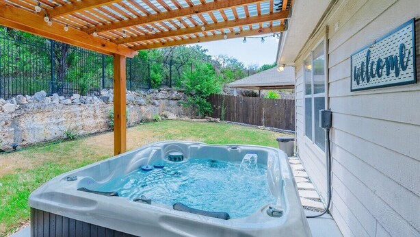 Een hottub onder een houten pergola in een achtertuin met een stenen muur en een houten schutting.