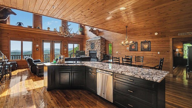 A spacious kitchen with a large island, wooden ceiling, and a stone fireplace.
