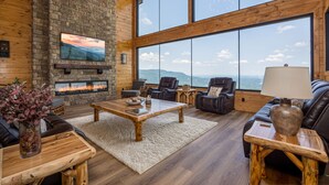 A spacious living room with a stone fireplace, large windows, and a view of the mountains. - Outdoor Games, Indoor Games, Incredible Views (SEVIERVILLE)