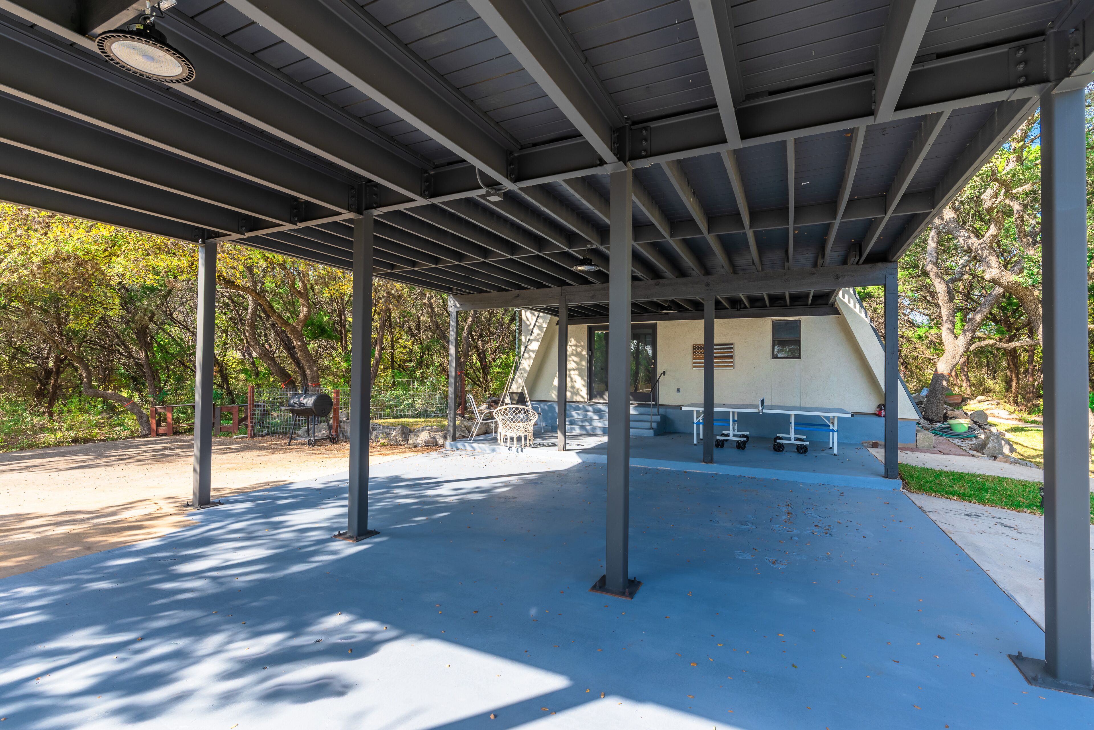Un espace extérieur abrité, doté de poutres métalliques, d’un sol en béton et d’une table de pique-nique.