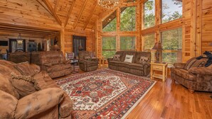A log cabin interior with wooden walls and ceilings, large windows, and a central rug. - Large Living Area| Game Room| Secluded| Easy Access (SEVIERVILLE)