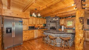 A wooden cabin interior with a central island, bar stools, a refrigerator, and stone accents. - Large Living Area| Game Room| Secluded| Easy Access (SEVIERVILLE)