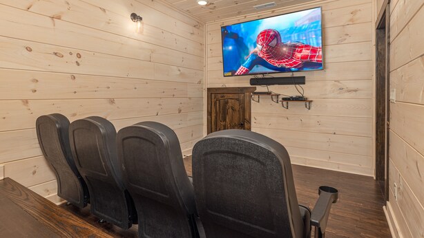 A wooden-paneled room with a flat-screen TV mounted on the wall, a wooden door, and four black chairs arranged in front. - Pigeon Forge*Resort*Dogs Welcome*Sleeps 12*Dollywood (SEVIERVILLE)