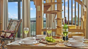 Ein Holzespeisetisch mit weißen Tellern, Schüsseln und einer Weinflasche, vor einer malerischen Kulisse mit Holzbalkonen und Blick ins Freie.