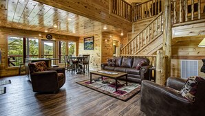 Ein Holzblockhaus-Interieur mit einer Holztreppe, einem Ledersofa, einem Couchtisch und einem Essbereich.