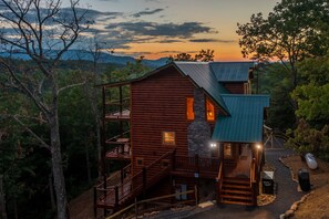 Une cabane en rondins avec une cheminée en pierre, une terrasse en bois et une vue sur la forêt environnante.