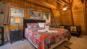 Ein gemütliches Schlafzimmer mit Holzbalkendecke, einem großen Bett mit Steppdecke, zwei Fenstern, einem Nachttisch und einer Bank.
