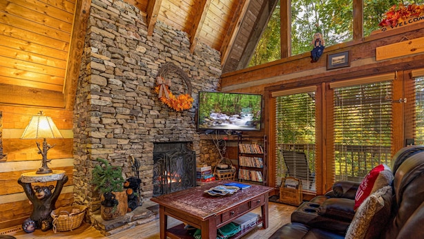Ein gemütliches Blockhauskaminzimmer mit Kamin, Fernseher, Bücherregal und einer Ledersofa.