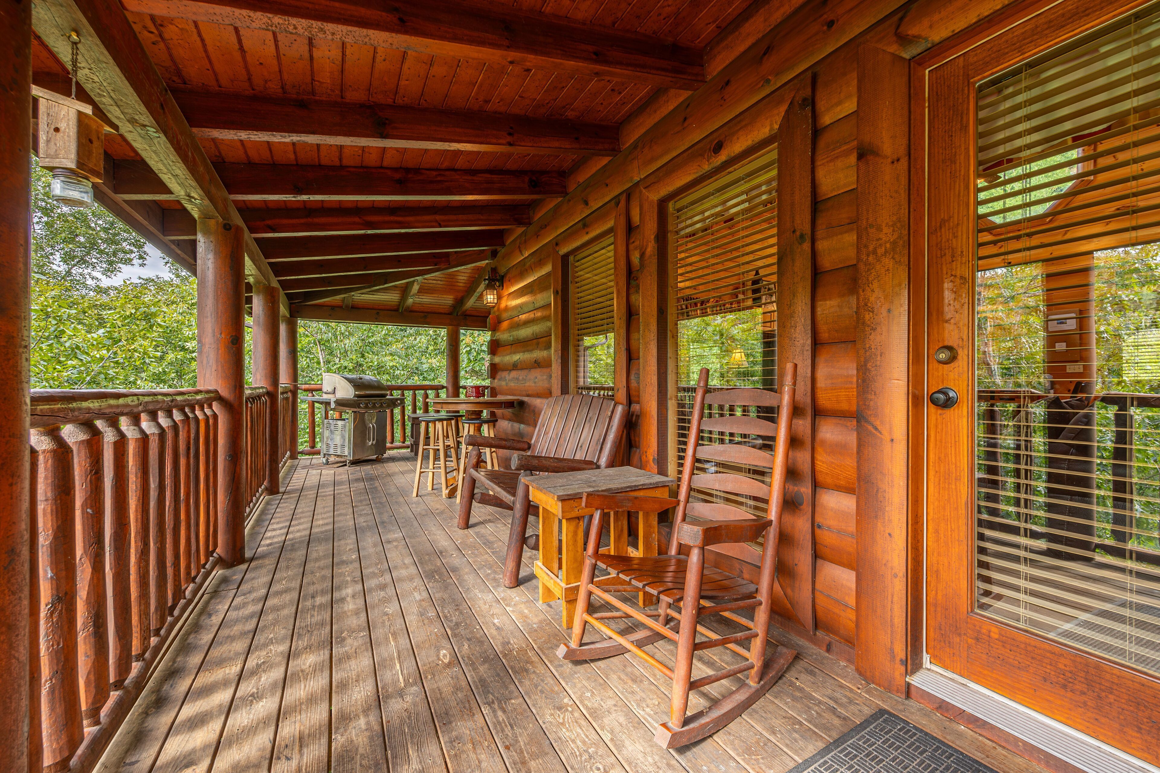 A wooden porch with rocking chairs, a table, and a door with blinds.