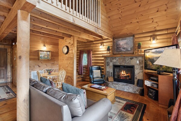 A cozy log cabin interior with a fireplace, leather sofa, and wooden walls. - Caught Up In Mountain Relaxation (PIGEON FORGE)