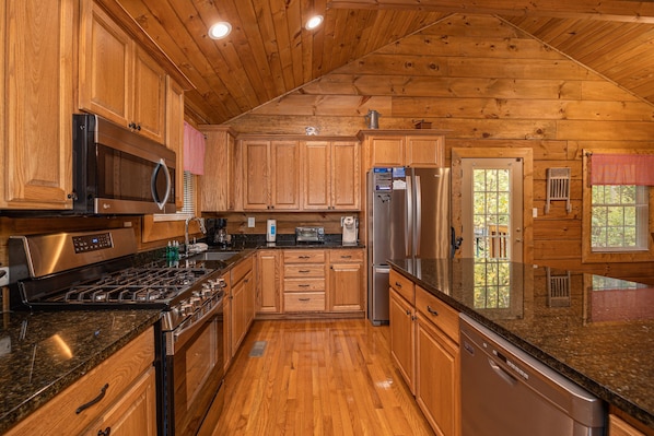 Una cocina con gabinetes de madera, electrodomésticos de acero inoxidable, encimeras de granito y techo de madera.