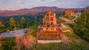 Ein zweistöckiges Holzhaus mit einer Terrasse, umgeben von Bergen und viel Grün.