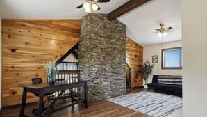 A room with a stone fireplace, wooden walls, a dining table with chairs, a sofa, and ceiling fans.