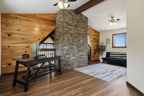A room with a stone fireplace, wooden walls, a dining table with chairs, a sofa, and ceiling fans. - Level Up From Luxury & Incredible Mountain Views (SEVIERVILLE)