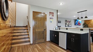 A modern kitchen with wooden flooring, a built-in dishwasher, and a wooden staircase leading to another level.
