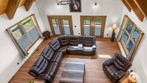 Un salón amplio con un sofá seccional grande, suelo de madera y ventanas grandes con contraventanas.