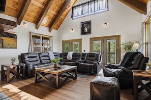 A spacious living room with leather sofas, a wooden coffee table, and large windows offering views of greenery.