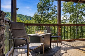 An outdoor patio with a grill, two chairs, and a view of a forested area.