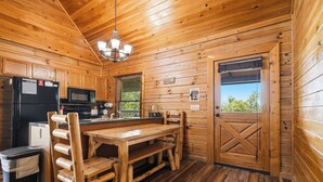 Cocina rústica de cabaña con una mesa de comedor, sillas, un refrigerador, microondas y ventana con vistas.