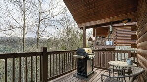 Eine Holzterrasse mit Grill und Korbstühlen, mit Blick auf eine gebirgige Landschaft.