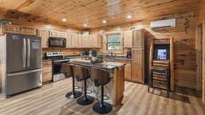A wooden cabin-style kitchen with a refrigerator, microwave, stove, and bar stools. - Near The Golf Corse, On The Creek (COSBY)