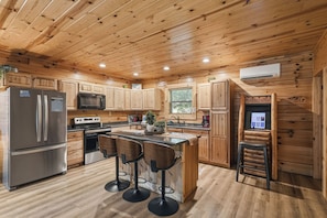 A wooden cabin-style kitchen with a refrigerator, microwave, stove, and bar stools. - Near The Golf Corse, On The Creek (COSBY)