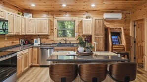 A wooden cabin interior with a kitchen featuring wooden cabinets, a stainless steel dishwasher, a granite countertop, and a central island with seating. - Near The Golf Corse, On The Creek (COSBY)