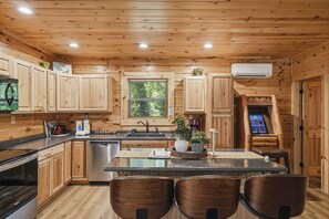 A wooden cabin interior with a kitchen featuring wooden cabinets, a stainless steel dishwasher, a granite countertop, and a central island with seating. - Near The Golf Corse, On The Creek (COSBY)