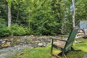A wooden bench by a stream in a forested area with a small shed in the background. - Near The Golf Corse, On The Creek (COSBY)