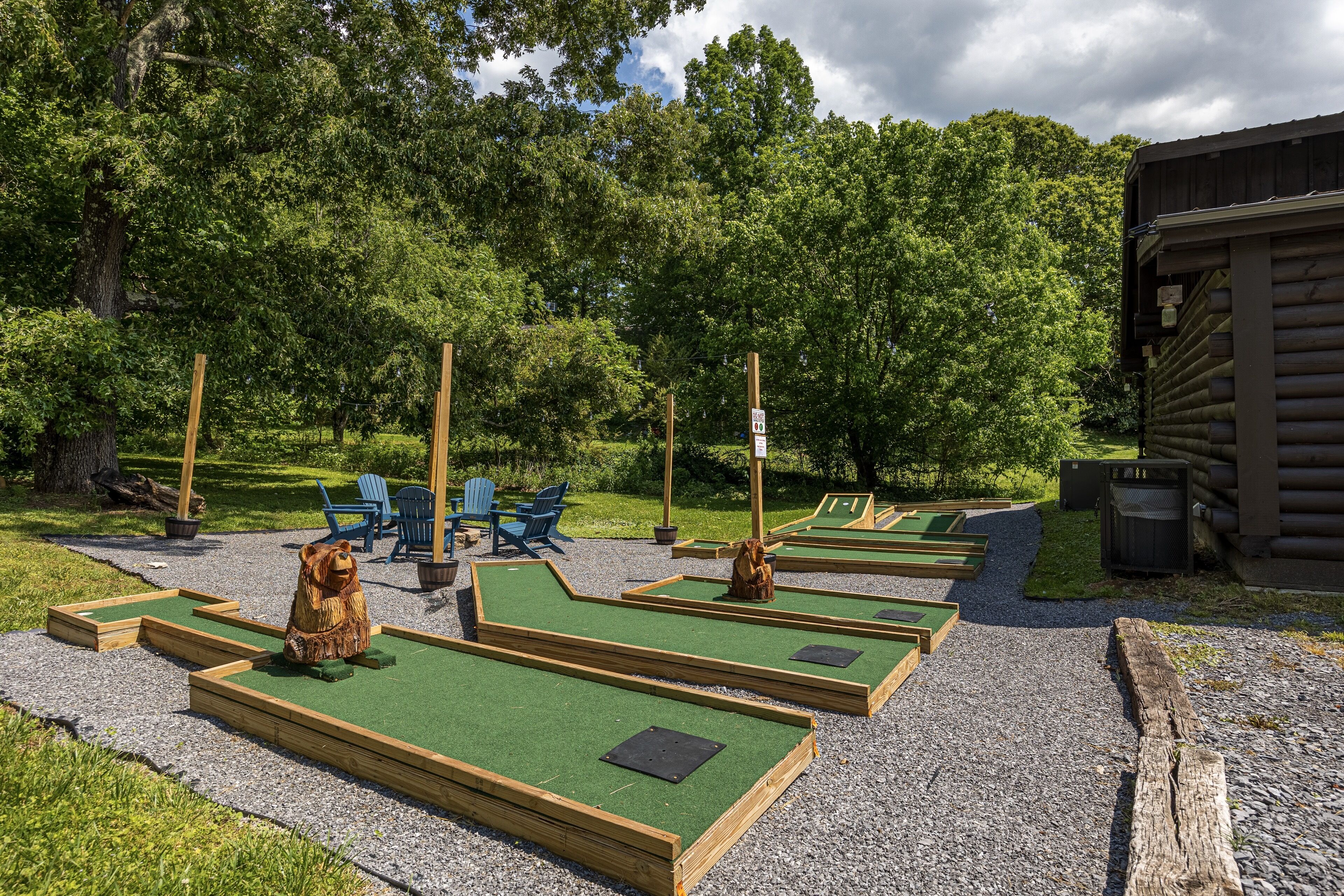 Des parcours de mini-golf avec des structures en bois et un gazon vert, entourés d’arbres et d’un bâtiment en bois.